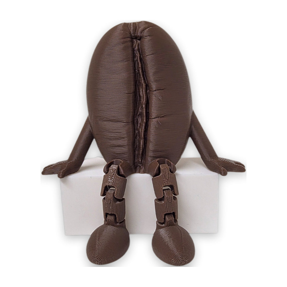 Articulated coffee bean buddy sitting on a shelf edge with legs hanging