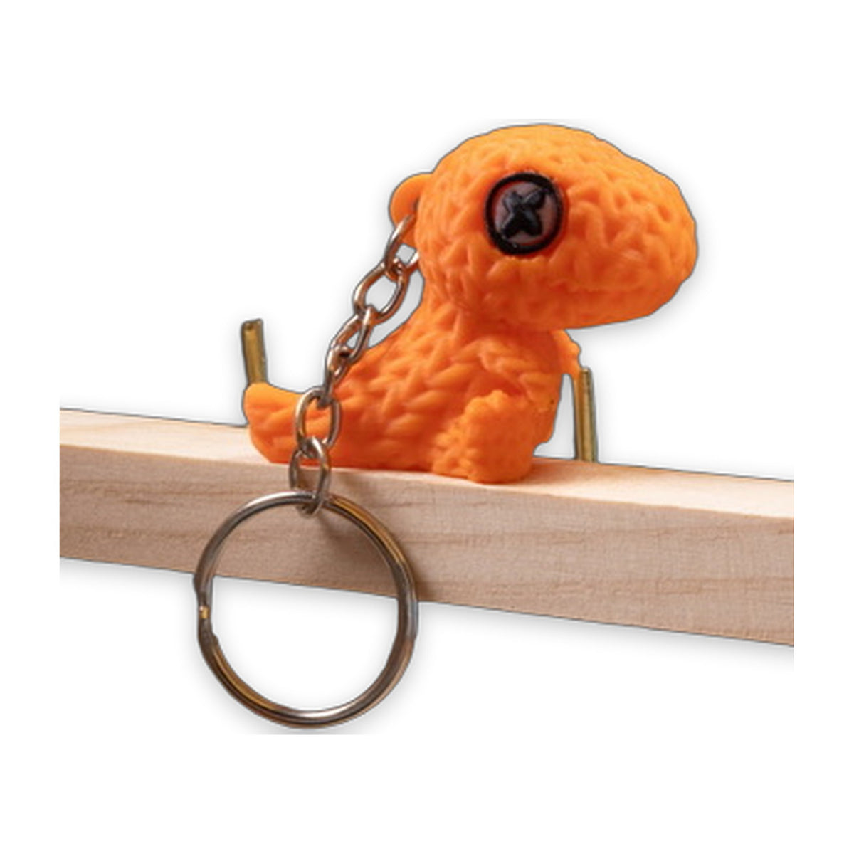 Orange textured dinosaur keychain perched on a wooden edge